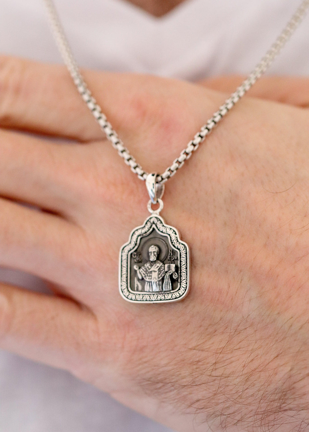 Silver pendant necklace on a hand with a blurred background