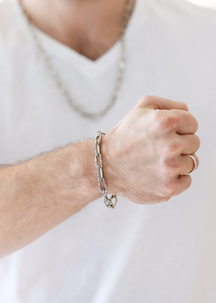 Person wearing a silver chain bracelet on a plain background (Zalori)