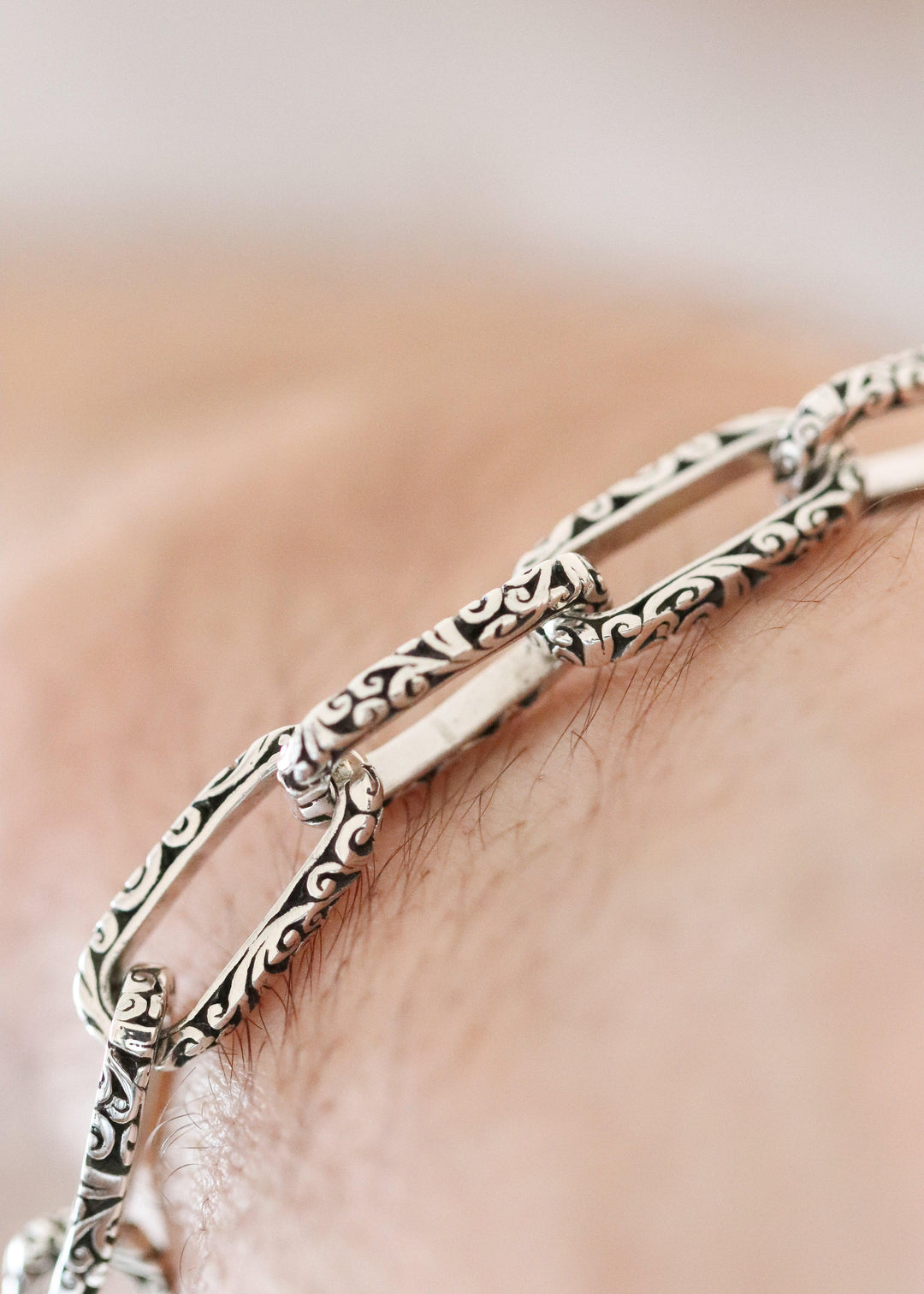 Silver bracelet with intricate designs on a person's wrist against a neutral background