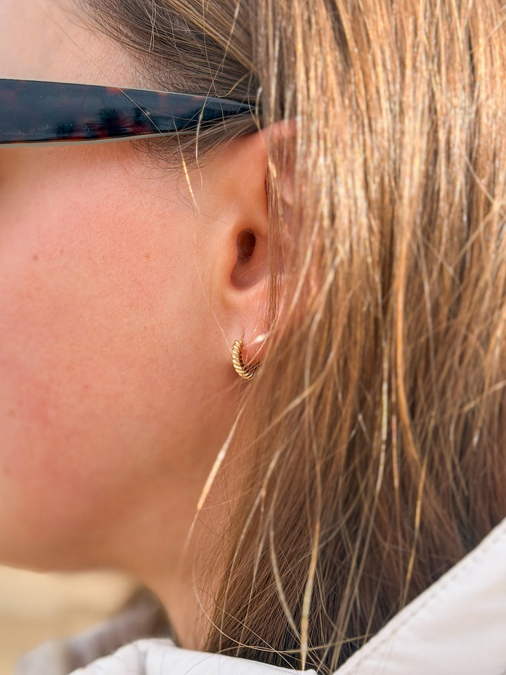 Close-up of a person wearing gold hoop earrings with sunglasses on.