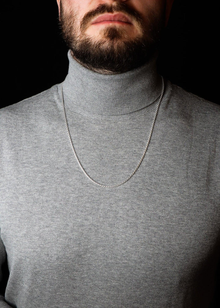 Man wearing a gray turtleneck sweater with a necklace against a black background