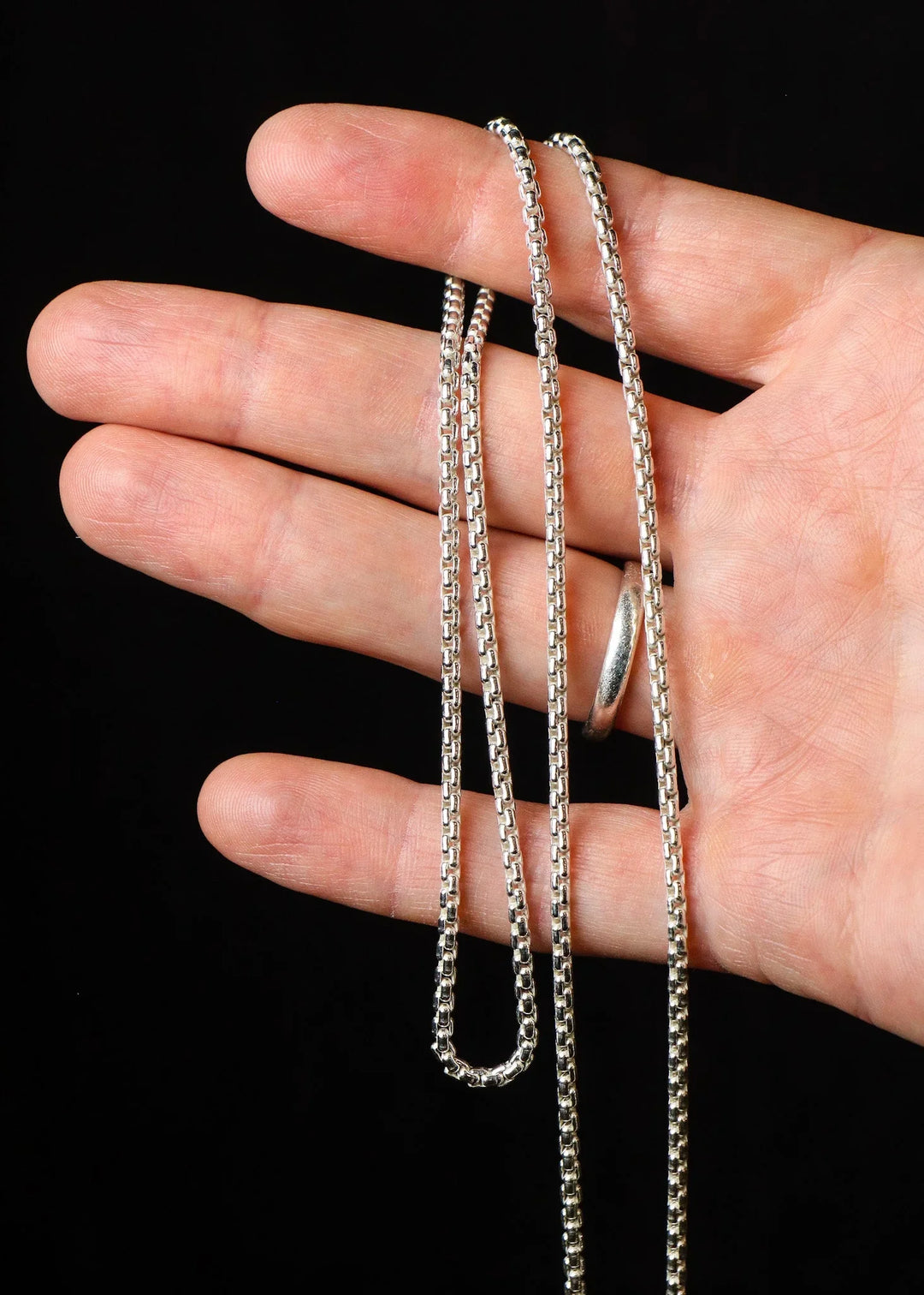Hand holding two silver chains against a black background